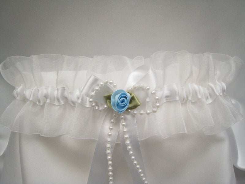 Photo of a wedding garter made from Organza ribbon and has a bow and rose Stitched In the front.